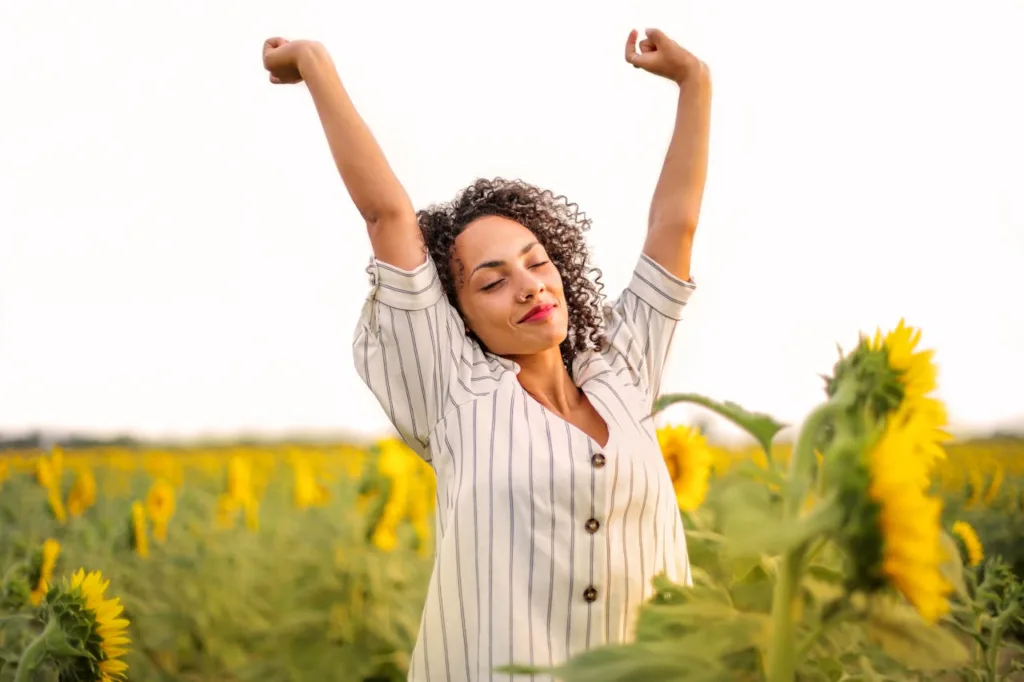 woman in field of flowers raising arms triumphantly